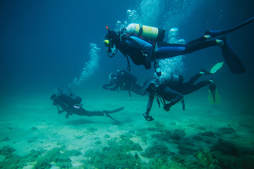 Group of divers underwater with scuba equipment and two of them with action cameras.