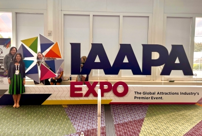 Three women to the left of a huge IAAPA Expo sign