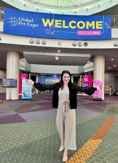 Woman in a greeting pose in front of a Welcome sign at a trade show